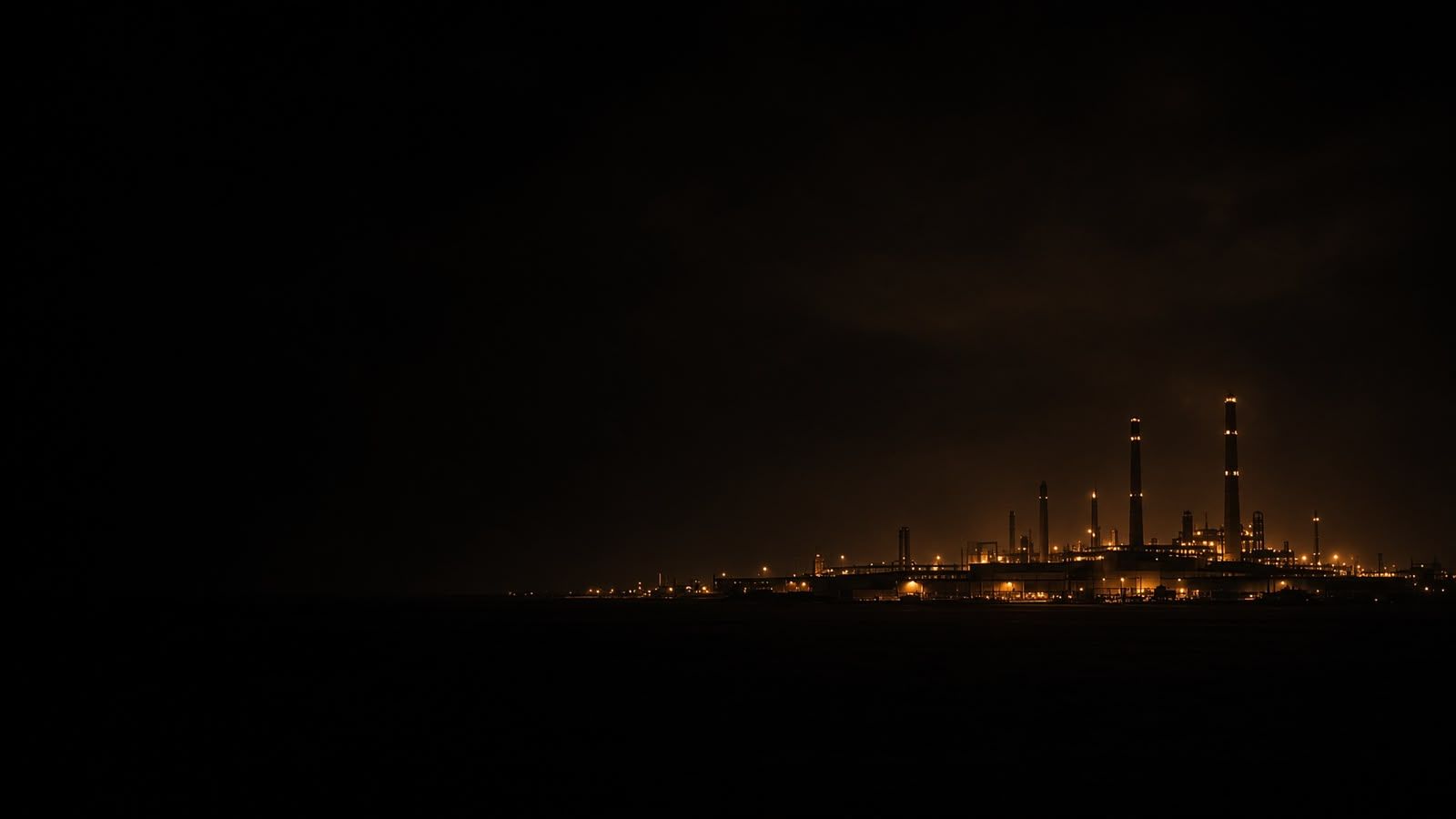 Planta industrial iluminada de noche, vista a lo lejos.